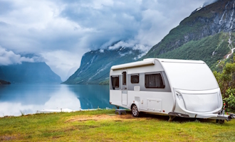 a caravan parked beside a scenic lake and mountains